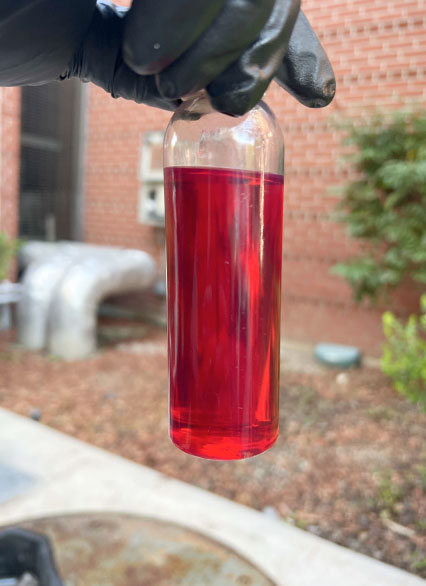 Sample of Red Liquid in Glass Bottle Held by Gloved Hand